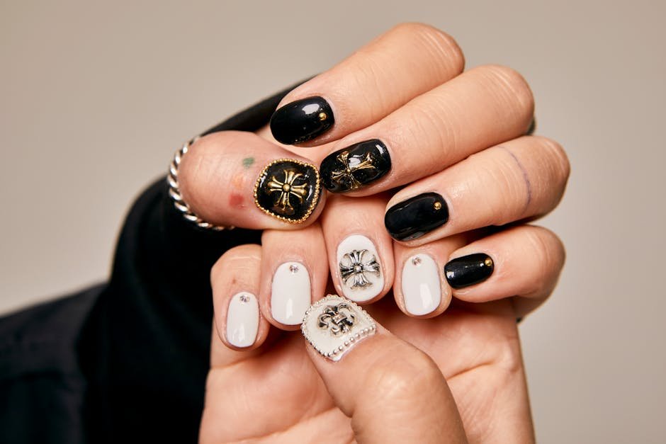 Close-up of women's hands showcasing artistic black and white nail art with ornate embellishments.