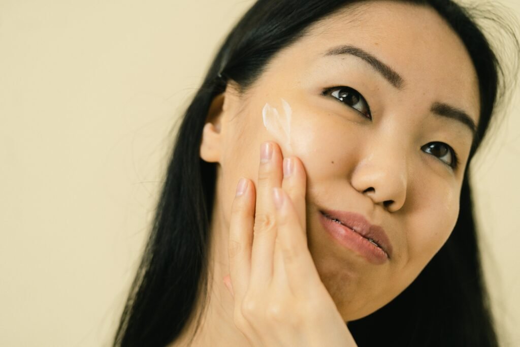 Woman with long black hair applying facial cream in studio. Focus on skincare and beauty routine.